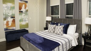 A modern bedroom with a large bed, two side tables, abstract wall art, and a bench.