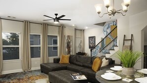A modern living room with a sectional sofa, a dining table set for four, and a staircase with a railing.