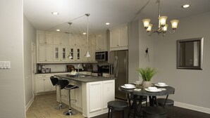 A modern kitchen with white cabinets, stainless steel appliances, and a dining area with a round table and bar stools.
