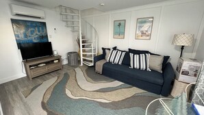 Ein Wohnzimmer mit einem dunkelblauen Sofa, einem Flachbildfernseher, einer Wendeltreppe und einem gemusterten Teppich.