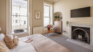 A bedroom with a large bed, a dresser, a chair, a fireplace, and a television.
