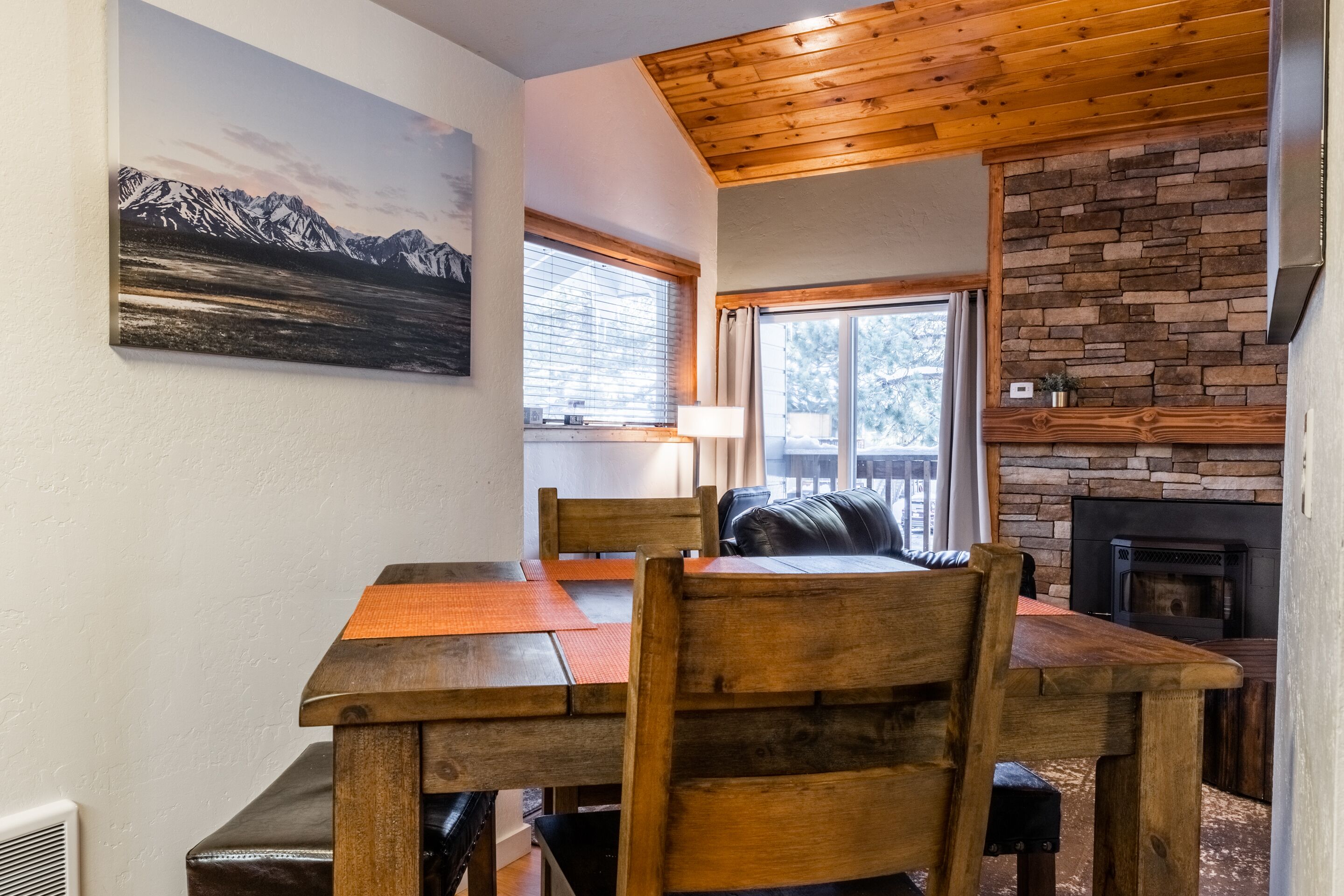 A wooden dining table with chairs, a fireplace, and a mountain painting on the wall.