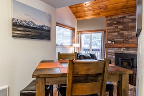 A wooden dining table with chairs, a fireplace, and a mountain painting on the wall.