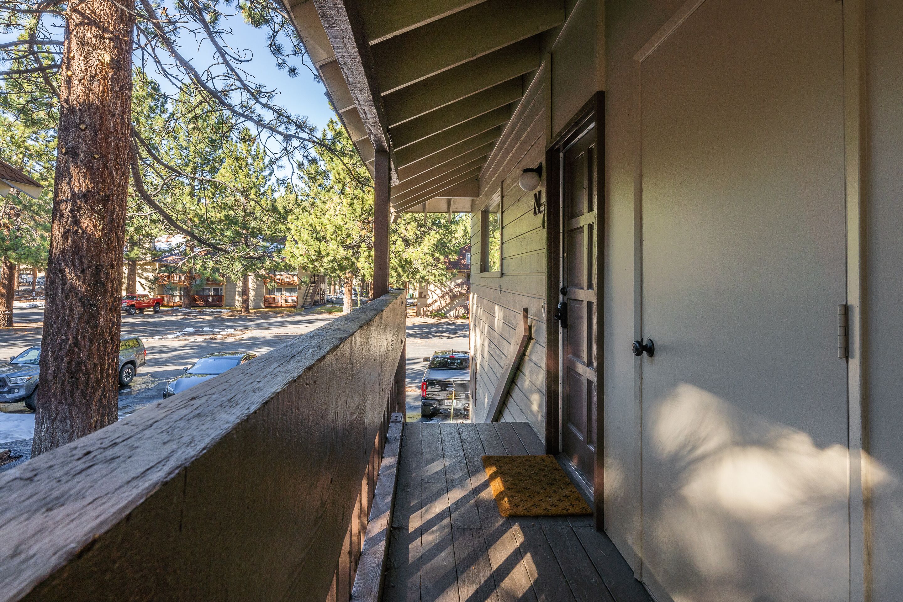 A covered porch with a wooden railing, a door, and a small mat on the ground.