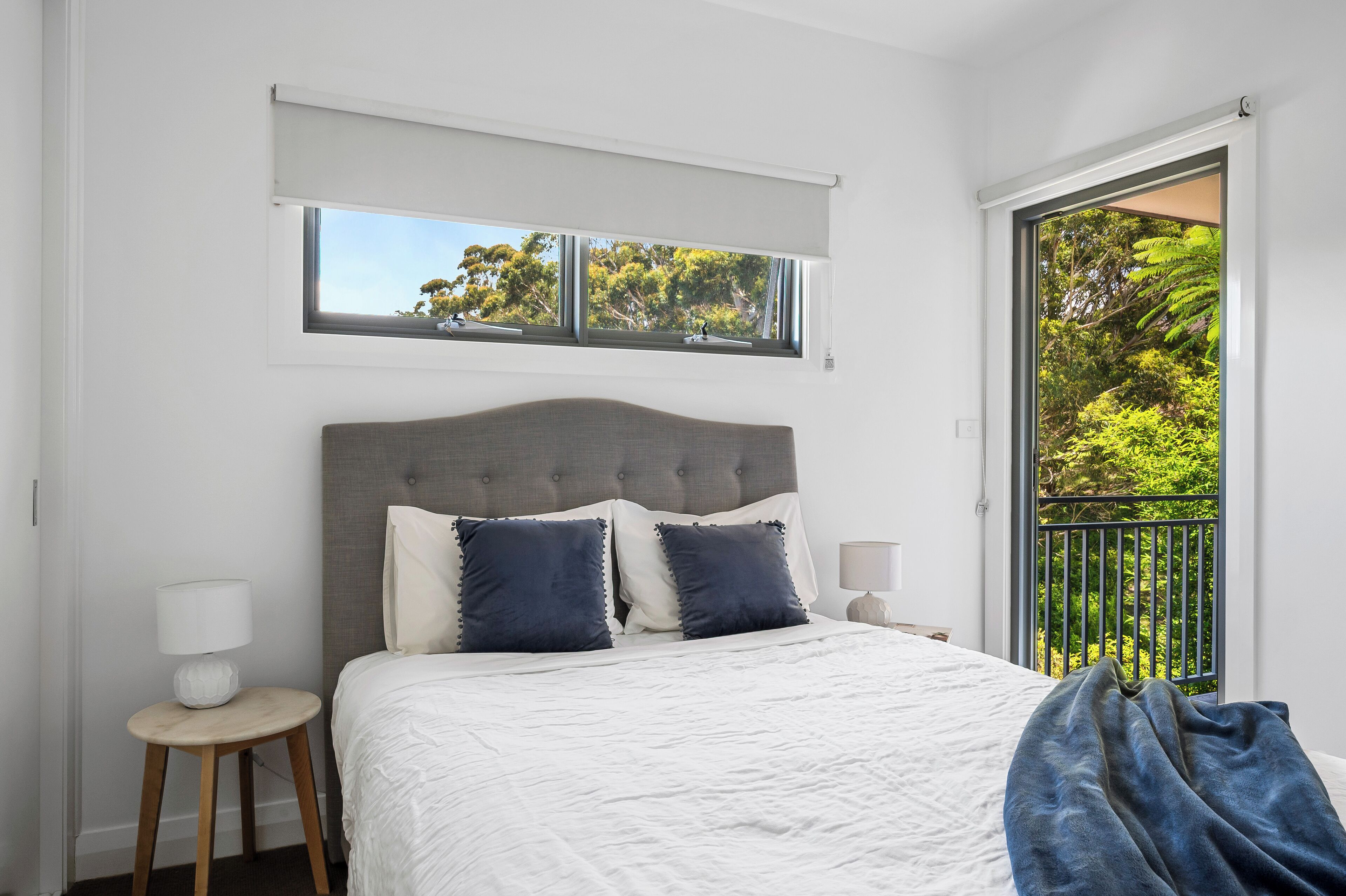 A bedroom with a bed, a window with a view of trees, and a balcony with a railing.