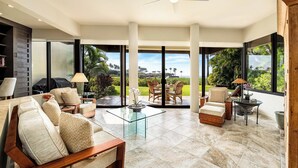 A spacious living area with a large glass door leading to a balcony, furnished with sofas, chairs, and a coffee table. - 🏖️Updated Ground Floor Mauna Lani Condo on the Golf Course (Kamuela)