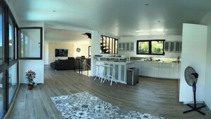 Una cocina moderna con una isla central, taburetes de bar y una zona de comedor con sofá y televisor.