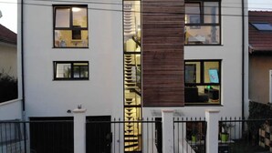 Un edificio moderno de dos pisos con amplios ventanales, un panel vertical de madera en el centro y una entrada con rejas.
