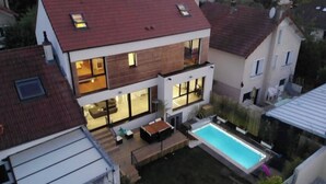 Una casa moderna de dos pisos con un amplio ventanal, una terraza de madera y una piscina.