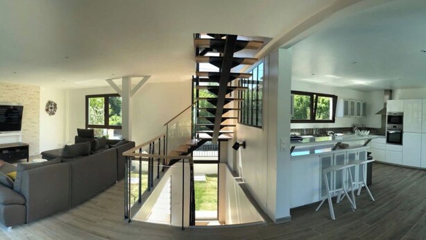 Un interior moderno con una escalera espiral central, una sala de estar con sofá y una cocina con armarios blancos.
