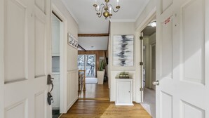A hallway with wooden flooring, white doors, a chandelier, and a large abstract painting on the wall.