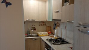 Una cocina con armarios de madera clara, una estufa a gas, un fregadero y un reloj en la pared.