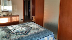 Un dormitorio con cama, cómoda y espejo. Se ve una puerta que da a otra habitación.