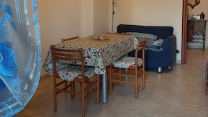Un comedor con una mesa cubierta con mantel floral, sillas de madera, un sofá azul, una lámpara de pie y un cuadro en la pared.