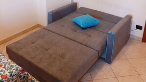 Una habitación compacta con sofá cama plegable, una lámpara de pie y una obra de arte enmarcada en la pared.