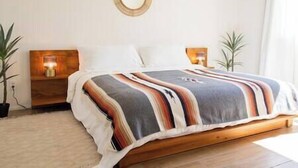 Een slaapkamer met een houten bed, gestreept beddengoed, twee nachtkastjes met lampen en een ronde spiegel aan de muur.