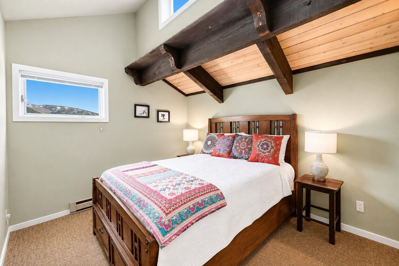 Une chambre à coucher avec un lit en bois, une table de chevet, deux lampes fixées au mur et une fenêtre donnant sur une montagne.