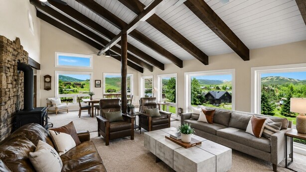 A spacious living room with a stone fireplace, leather furniture, and large windows offering a view of the countryside. - Pet Friendly, Great Views, Great For Large Groups (Crested Butte)