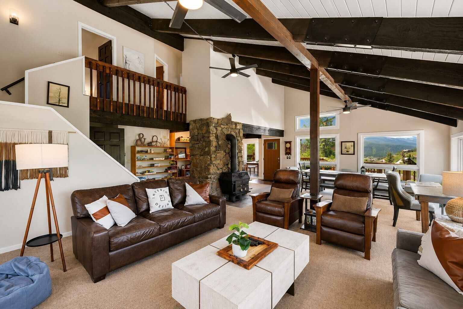 Amplia sala de estar con chimenea de piedra, muebles de cuero y vistas al exterior.
