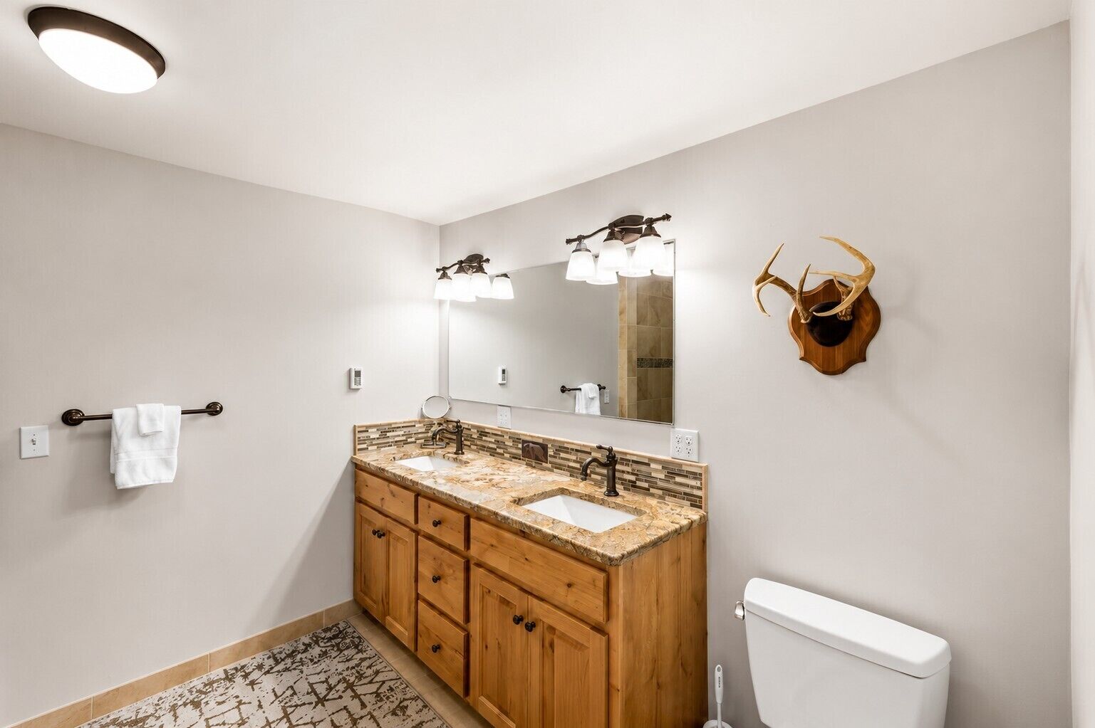 A bathroom with a wooden vanity, two sinks, a large mirror, and a wall-mounted toilet.