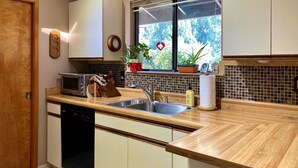 Una cocina con encimera de madera, pileta de acero inoxidable y ventana con vista a follaje.