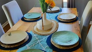 Una mesa de comedor con seis platos, un florero con flores y un cuadro en la pared.