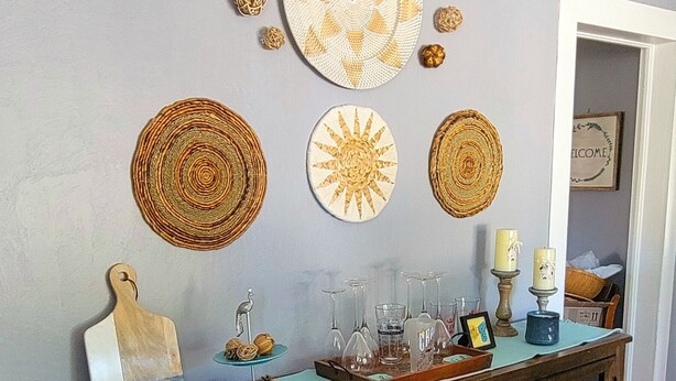 Una consola de madera con cristalería y objetos decorativos frente a una pared con tapices tejidos.