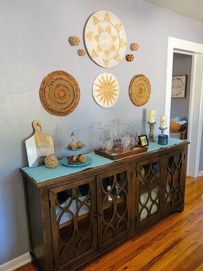 A wooden console table with glassware and decorative items against a wall with woven wall hangings. - Jennywood Cottage - Prescott Cabin Rentals (Prescott)