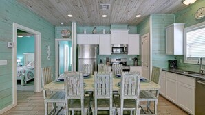 A kitchen with white cabinets, a stainless steel refrigerator, and a dining table with chairs. - Blue Wave~Community Pool~Family Friendly~Sleeps 10 (Port Aransas)