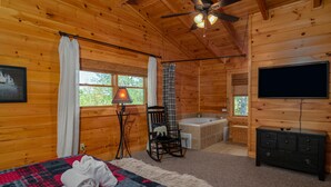 A wooden cabin room with a bed, a rocking chair, a bathtub, and a television. - Beautiful Autumn Season in The Smokies! Hot Tub! (Sevierville)