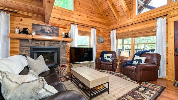 A cozy log cabin interior with a stone fireplace, leather sofas, a television, and a wooden ceiling. - Beautiful Autumn Season in The Smokies! Hot Tub! (Sevierville)