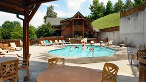 A wooden cabin with a pool surrounded by lounge chairs and a covered patio area. - Beautiful Autumn Season in The Smokies! Hot Tub! (Sevierville)