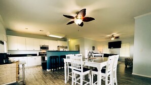 Una cocina amplia con armarios blancos, una isla central y un comedor con mesa y sillas blancas.