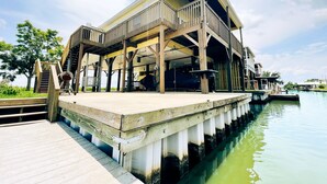 Un edificio frente al agua con una terraza de madera y un espacio cubierto.