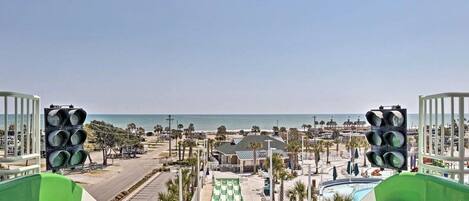 A view from a high vantage point overlooking a resort area with a pool, beach, and clear sky.