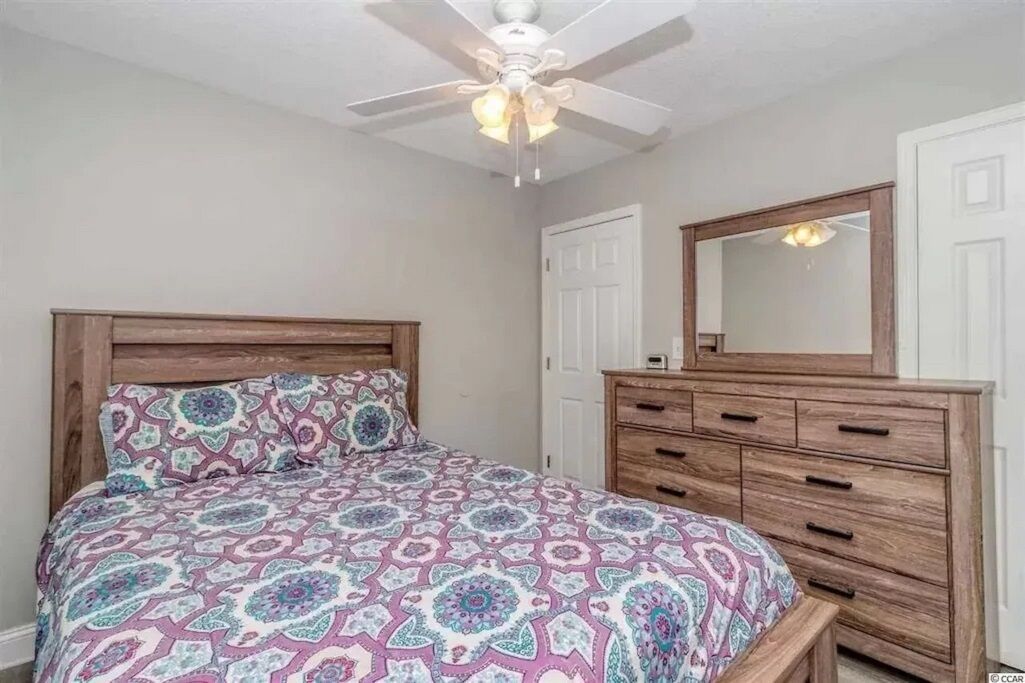 Une chambre à coucher avec un lit, une commode, un miroir et un ventilateur de plafond.
