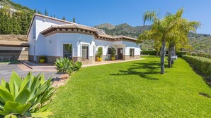 Une villa blanche, dotée d’un toit en tuiles, entourée d’une pelouse bien entretenue et agrémentée de quelques plantes en pot.