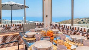 A dining table set with plates, glasses, and a fruit bowl, overlooking a coastal view. - Villa Universal Beauty Resort Torrox by Ruralidays (Málaga)