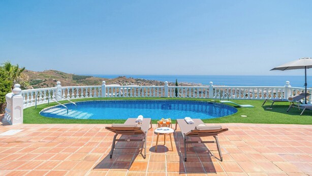 A swimming pool with a white fence, two lounge chairs, a table with drinks, and a view of the sea. - Villa Universal Beauty Resort Torrox by Ruralidays (Málaga)