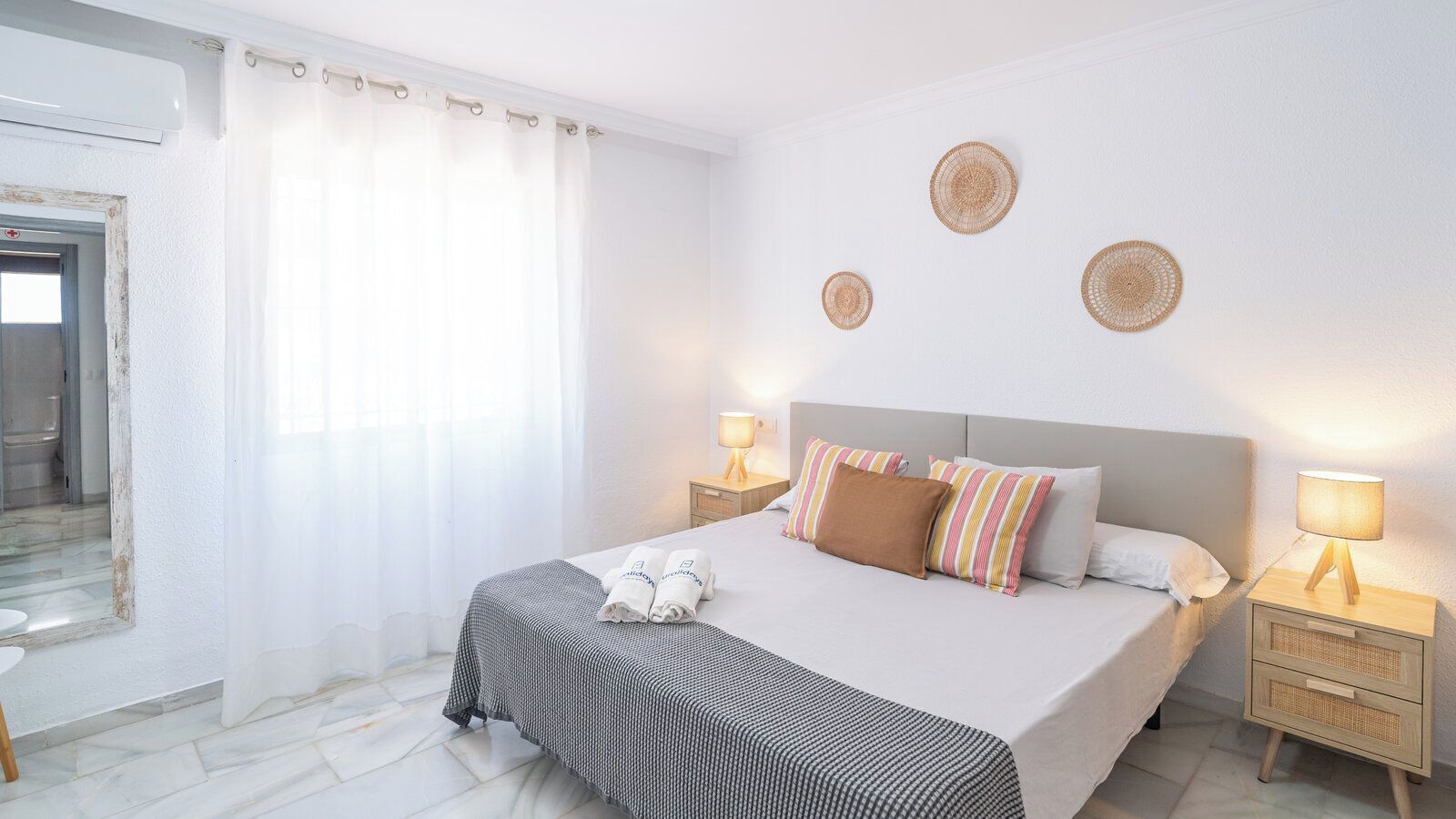 A neatly arranged hotel room with a bed, bedside tables, and a bathroom visible through a glass door.