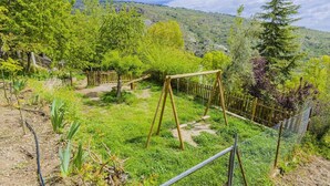 A garden with a wooden swing set, a fenced area, and a view of a hilly landscape. - Barranco de La Salud - El Porche Nevada by Ruralidays (Granada)