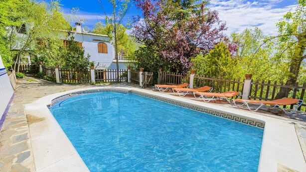 A rectangular swimming pool with a white tiled edge and a blue center, surrounded by a wooden fence and potted plants. - Barranco de La Salud - El Porche Nevada by Ruralidays (Granada)