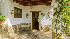 A stone patio with a round table, potted plants, and a wooden ceiling structure. - Barranco de La Salud - El Porche Nevada by Ruralidays (Granada)