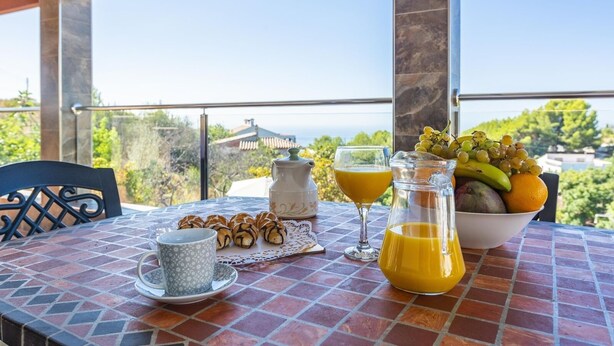 A table with croissants, a pitcher of orange juice, a bowl of fruit, and a cup of coffee on a tiled patio with a view of the sea. - Villa Alberto Frigiliana by Ruralidays (Málaga)