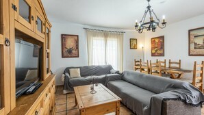A cozy living room with a sofa, a wooden dining table, and a TV. - Casa La Lomilla Canillas de Albaida by Ruralidays (Málaga)