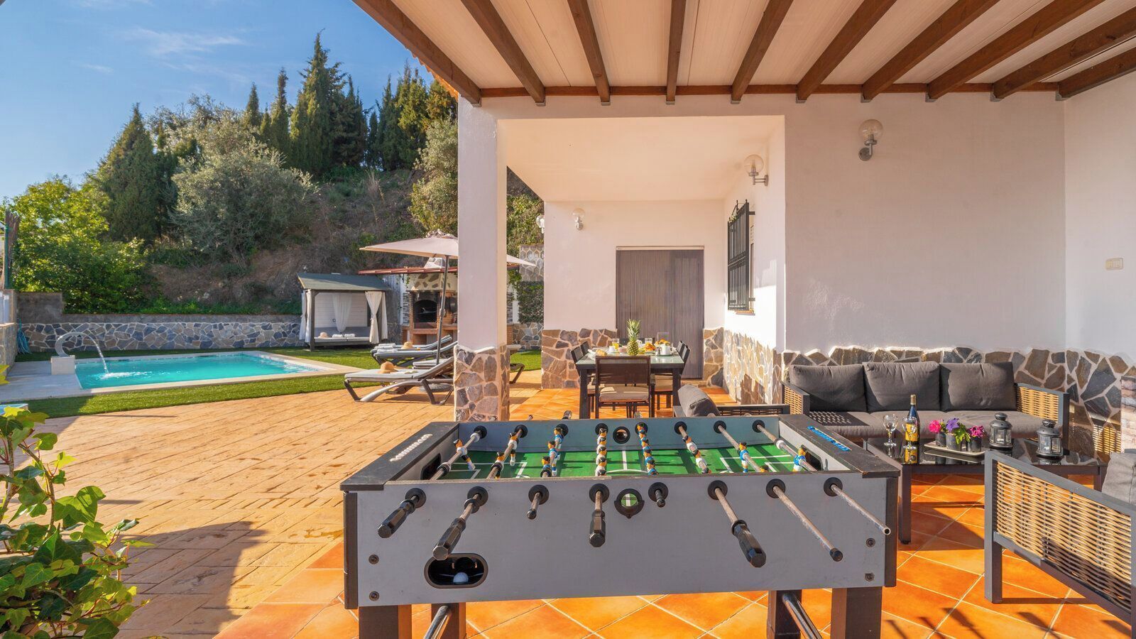 An outdoor patio with a foosball table, a pool, and a seating area with a sofa and table.