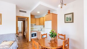 Un espacio habitable compacto con kitchenette, una zona de comedor con mesa y sillas de madera, y un pequeño sofá.