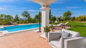 Ein Poolbereich mit einer weißen Säule, einem grauen Sofa und einer Rasenfläche mit Liegestühlen.