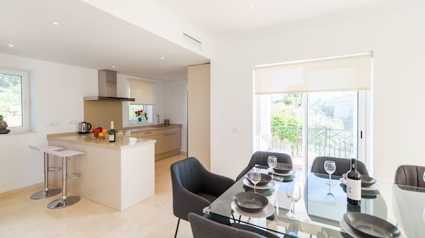 A modern kitchen with a central island, bar stools, and a dining area with a glass table and chairs. - Villa Latina Golf Arcos de la Frontera by Ruralidays (Cádiz)