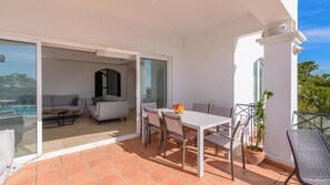 Ein Balkon mit Esstisch, Stühlen, einer Couch und einem Blumentopf.